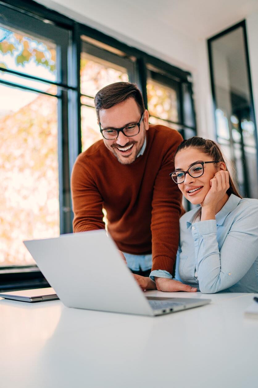 Male and female office workers smiling whilst looking at a laptop screen-min