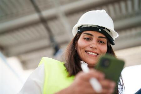 Woman wearing protective white helmet, using mobile phone at the construction site-1
